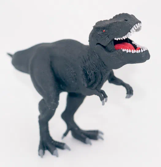 Modèle noir d'un dinosaure T-Rex avec la bouche ouverte, des dents blanches et une langue rouge, posé sur fond blanc.
