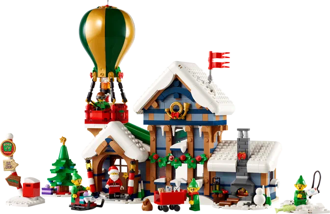 Une maison en bois bleue et blanche avec cheminée décorée pour Noël, Père Noël à l'entrée, des lutins verts autour, un ballon dirigeable vert et doré attaché au toit d'une annexe rouge.