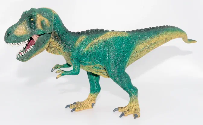 Un modèle de dinosaure Tyrannosaurus Rex vert avec des accents jaunes, bouche ouverte montrant ses dents pointues, posé sur un fond blanc uni.