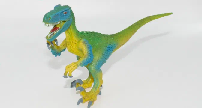 Jouet de dinosaure en plastique aux couleurs vert, bleu et jaune posé sur fond blanc.