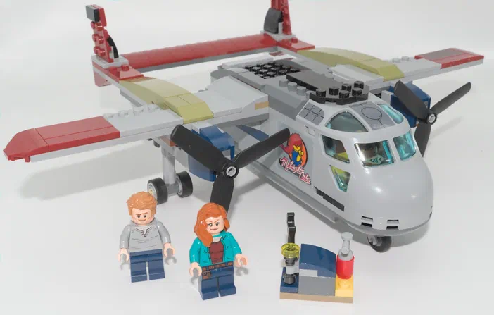 Un avion de transport en Lego gris avec des hélices noires et deux minifigurines debout devant.