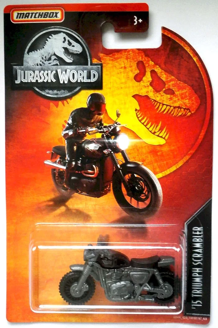 Carte Matchbox Jurassic World avec un modèle '15 Triumph Scrambler noir scellé dans une fenêtre plastique transparente en bas d'une carte orange illustrée par le logo du parc jurassique, la silhouette d'un dinosaure T-Rex et une image imprimée montrant un motard sur cette moto.