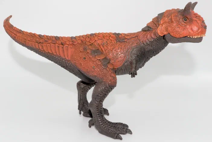 Un jouet de dinosaure à deux pattes avec une peau orange et grise sur fond blanc.