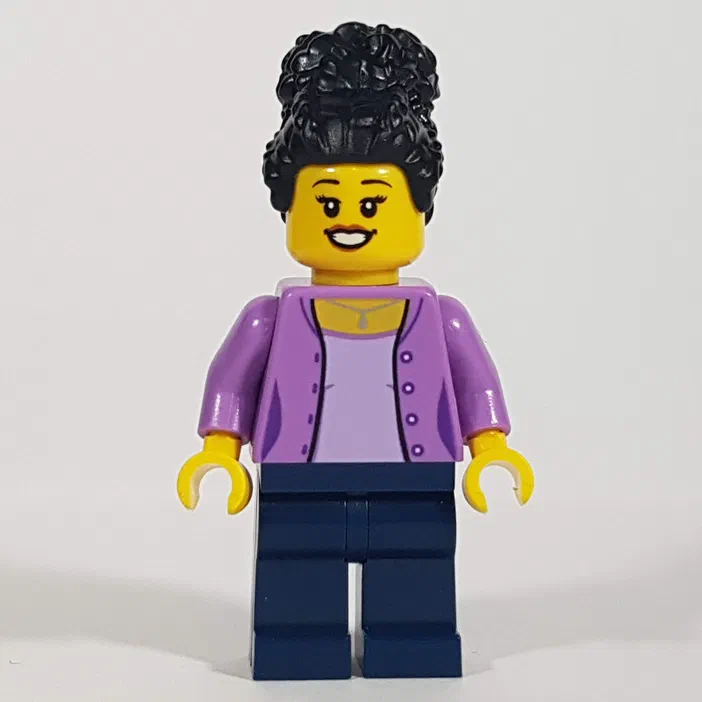 Une figurine LEGO féminine aux cheveux noirs bouclés coiffés en chignon haut, avec un visage jaune souriant, portant une veste violette claire boutonnée par-dessus un t-shirt pâle et des jambes bleues foncées sur fond blanc.