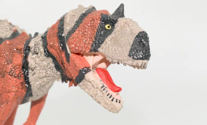 Un jouet de dinosaure à tête ouverte montrant une langue rouge, avec un corps rayé orange et gris.
