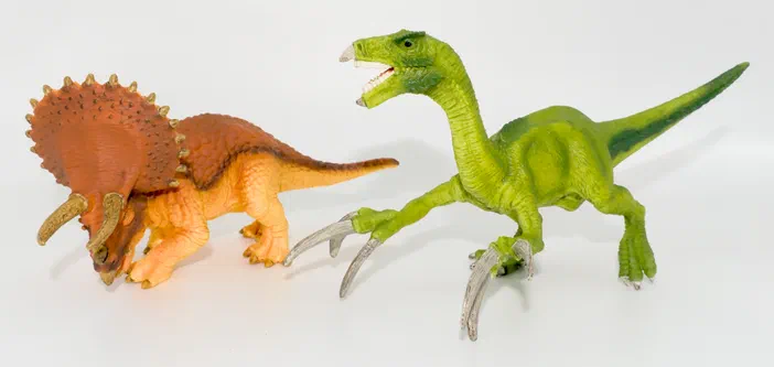 Deux figurines de dinosaures, un triceratope orange et un raptor vert, posés sur fond blanc.