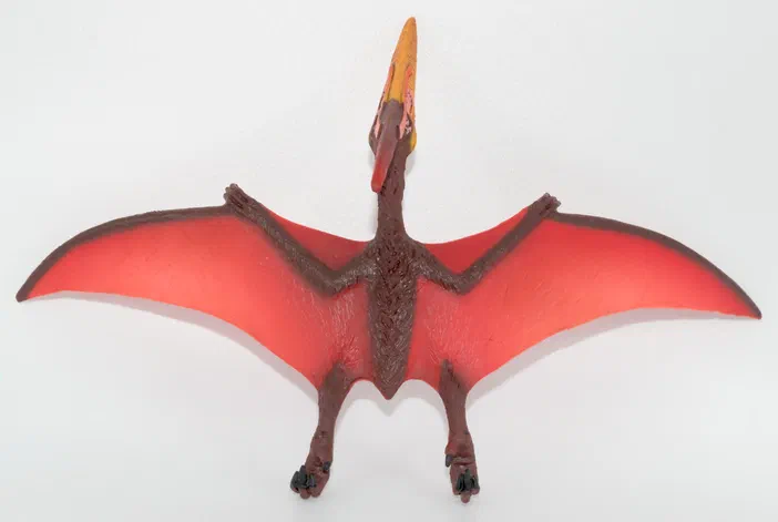 Jouet de dinosaure ailé rouge et marron sur fond blanc