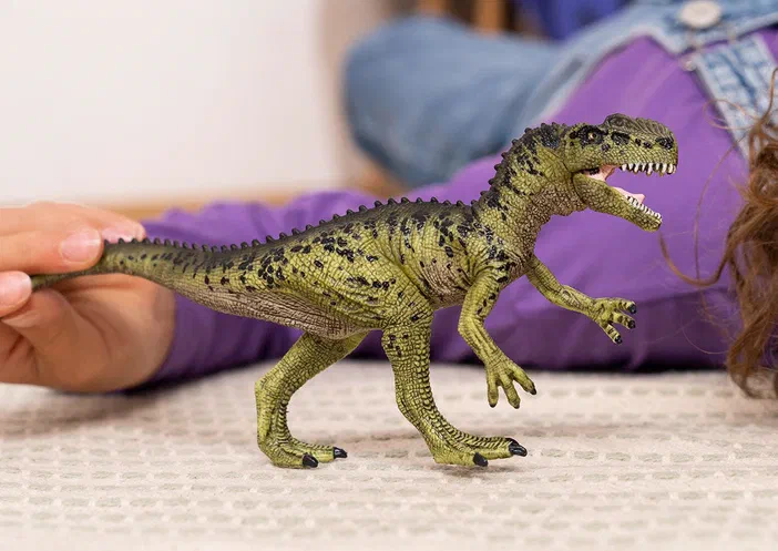 Une main tient un jouet de dinosaure vert et noir, le Monolophosaurus par Schleich.