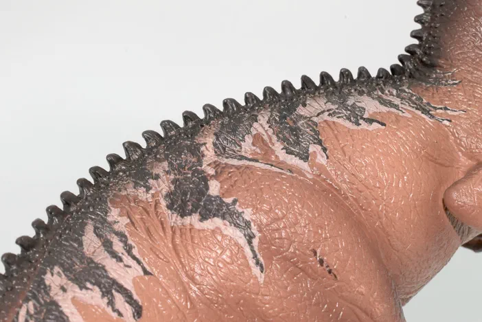 Vue rapprochée du dos d'un dinosaure jouet avec une crête de pointes sombres et des marques grises sur un corps rose.
