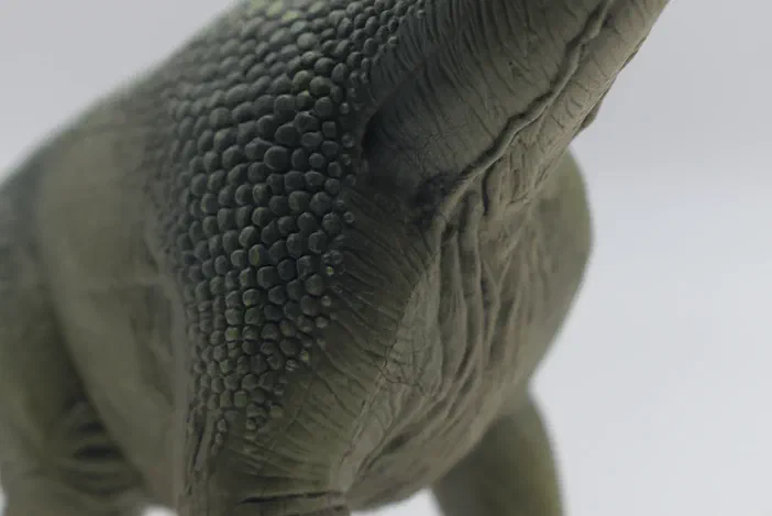 Vue rapprochée du dos d'un dinosaure en plastique vert avec une texture écailleuse détaillée.