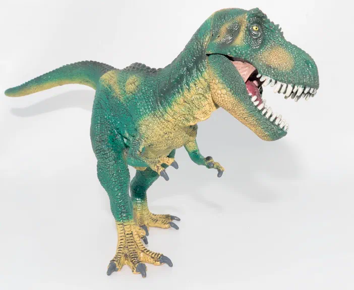 Un jouet de dinosaure T-Rex vert et jaune avec une bouche ouverte montrant des dents blanches.