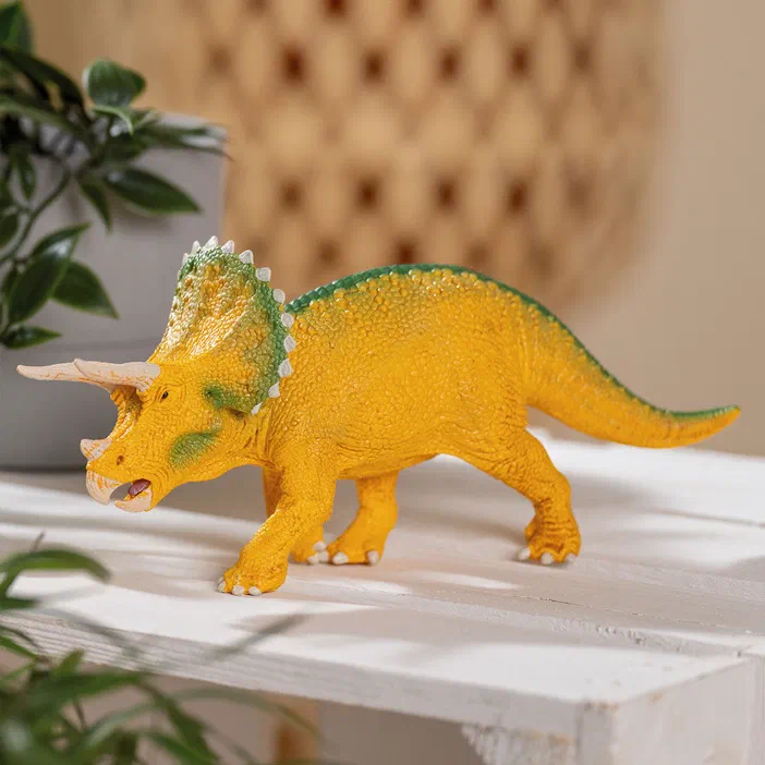 Figurine de tricératops jaune avec des accents verts sur le museau et la crête.