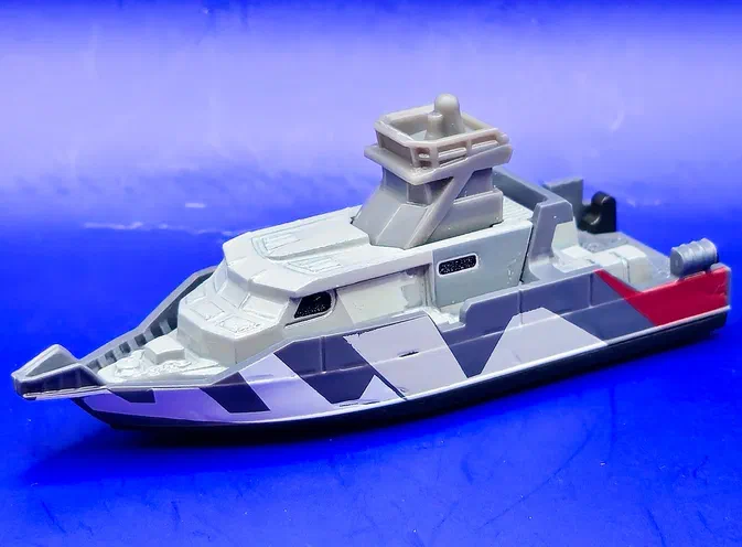 Bateau de patrouille en plastique gris et blanc avec des motifs géométriques noirs sur fond bleu.