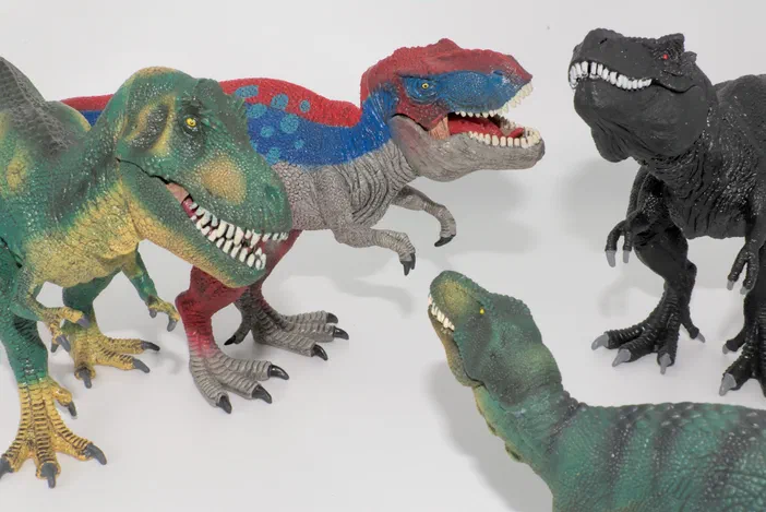 Cinq figurines de dinosaures, dont des T. rex et un Allosaurus, posées sur fond blanc.
