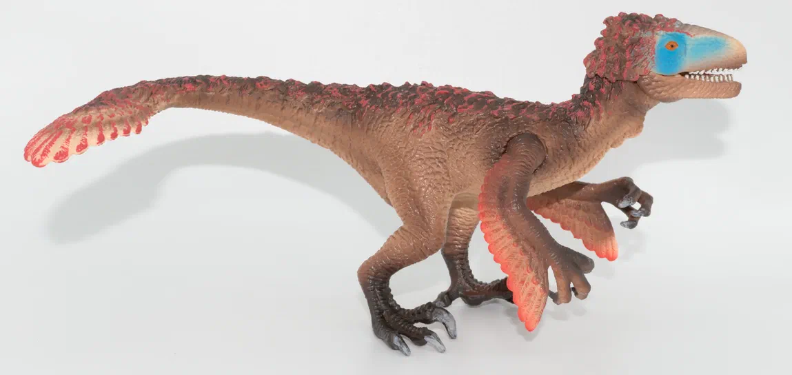 Figurine de dinosaure à deux pattes avec des ailes et une queue ornée de motifs rouges.
