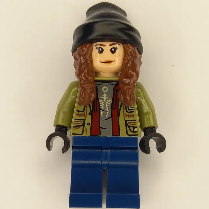 Minifigurine LEGO Jurassic World avec un bonnet noir, des cheveux bruns bouclés, une veste verte à motifs tribaux et un t-shirt gris orné d'un squelette.