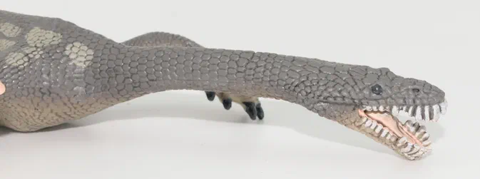 Maquette d'un dinosaure reptilien gris à la peau écailleuse, avec des taches claires sur le dos et une gueule ouverte montrant ses dents.
