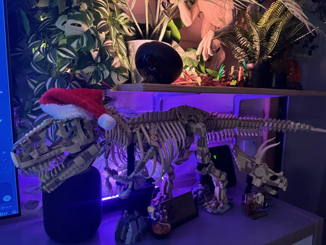 Un squelette de dinosaure en LEGO portant un bonnet rouge, entouré d'autres modèles et éclairé par des lumières violettes.