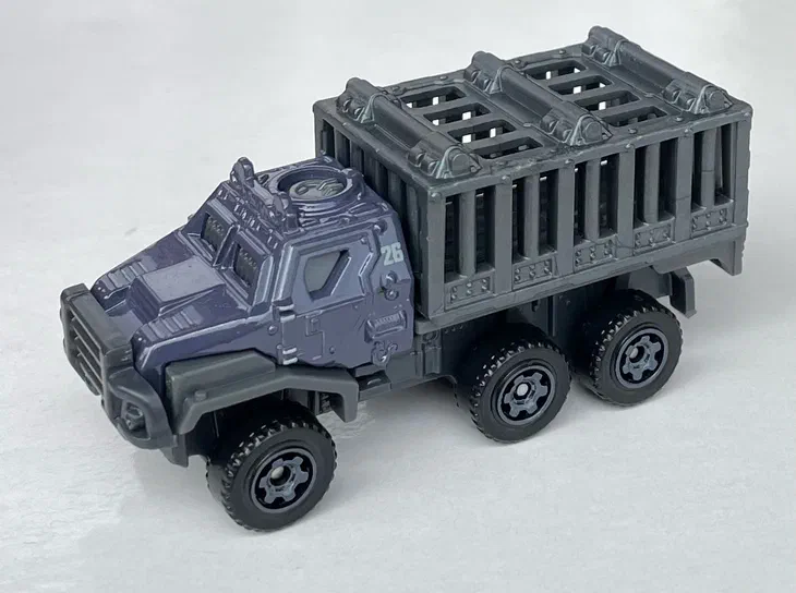 Voiture jouet Matchbox Armored Action Transporter de la série Jurassic Heroes JGY50 en gris foncé avec une remorque à barreaux.