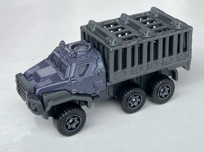 Voiture jouet Matchbox Armored Action Transporter de la série Jurassic Heroes JGY50 en gris foncé avec une remorque à barreaux.