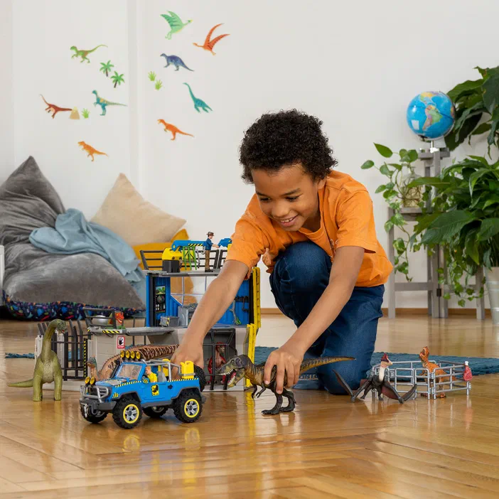 Un garçon joue avec des dinosaures et une voiture tout-terrain Schleich dans un salon.