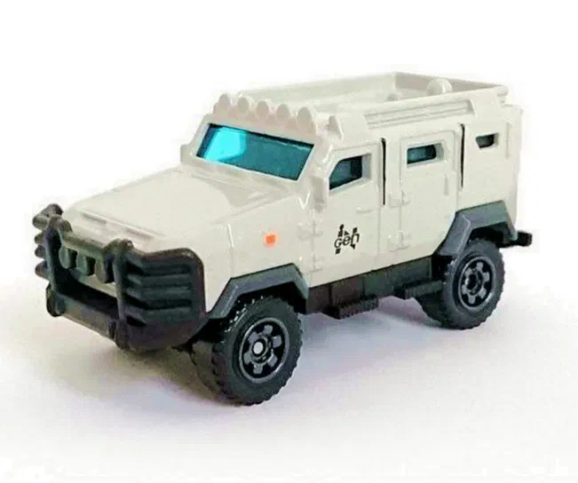 Petit camion jouet Matchbox Textron Tiger gris beige de la série Jurassic World avec des roues noires et un pare-brise bleu.