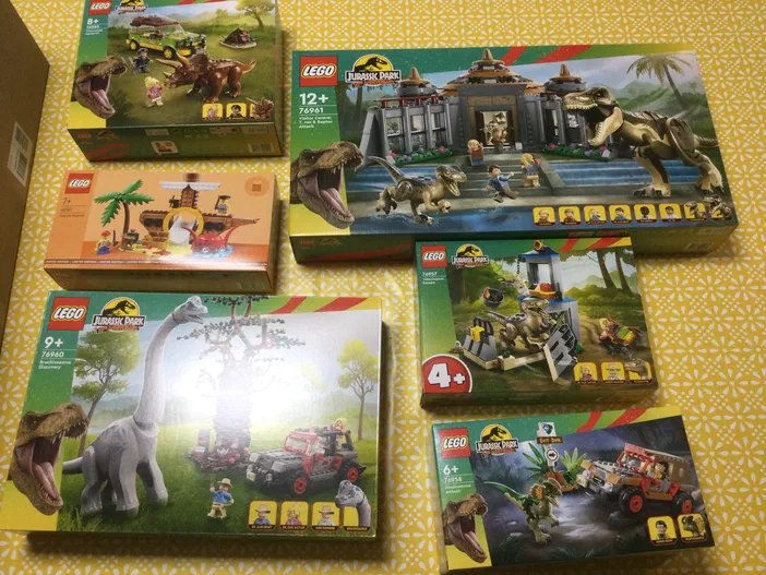 Une collection de boîtes de jeux LEGO Jurassic Park disposées sur un fond jaune à motifs.