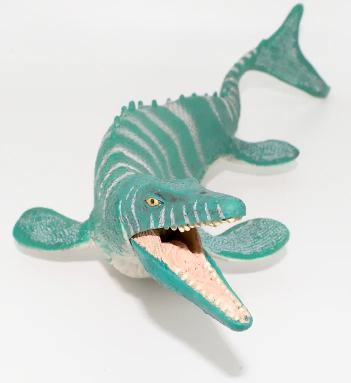 Un jouet de dinosaure en plastique vert avec des rayures blanches et une bouche ouverte.