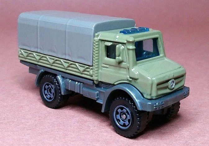 Puce Matchbox verte Mercedes-Benz Unimog U5023 avec remorque grise sur fond rose.