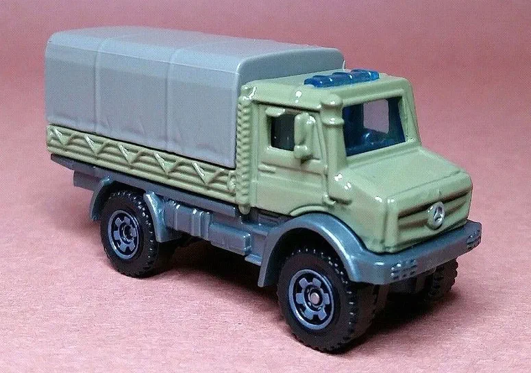 Puce Matchbox verte Mercedes-Benz Unimog U5023 avec remorque grise sur fond rose.