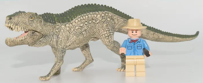 Un dinosaure à peau écailleuse et une figurine de minifigur en plastique posés sur un fond blanc.