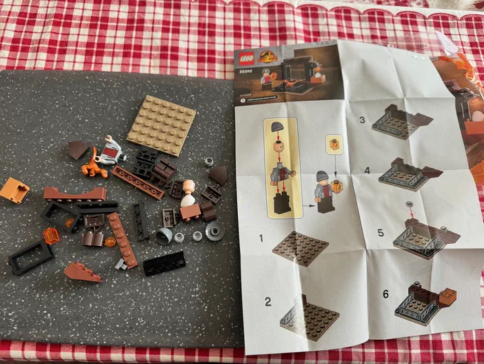Des pièces de LEGO Jurassic World et une instruction ouverte sur un fond à carreaux rouges.