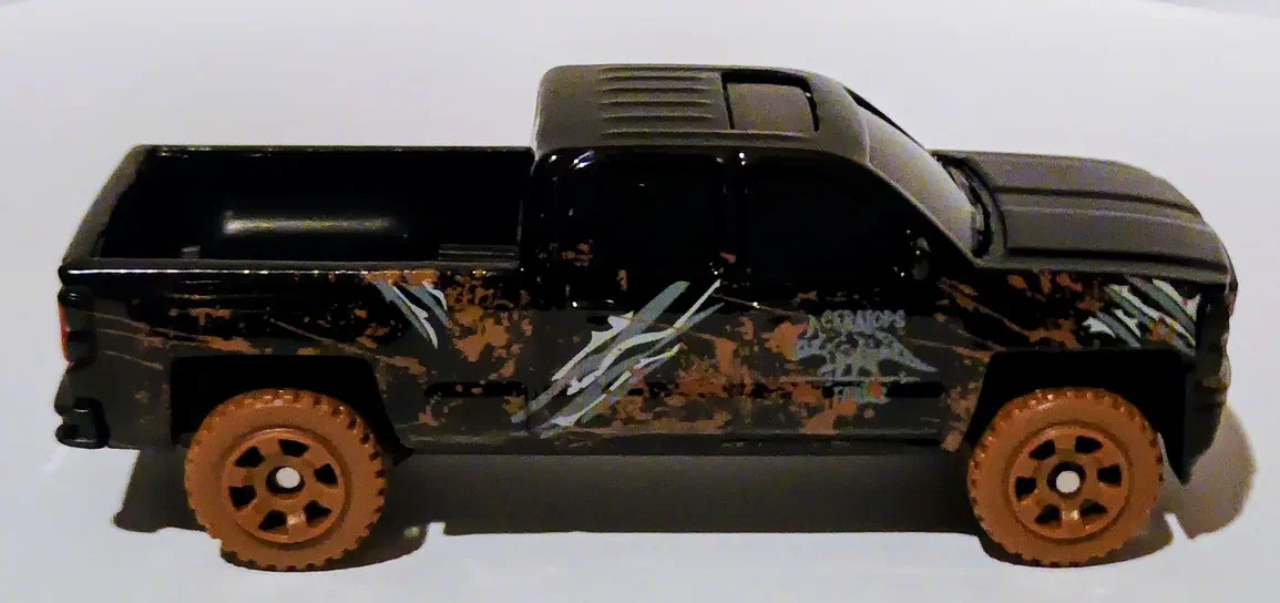 Camionnette Matchbox noire avec des motifs de dinosaures et une illustration d'un T-Rex sur le côté.