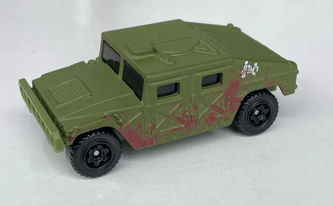 Voiture jouet Matchbox verte avec des traces de boue rouge et un logo InGen sur le côté.