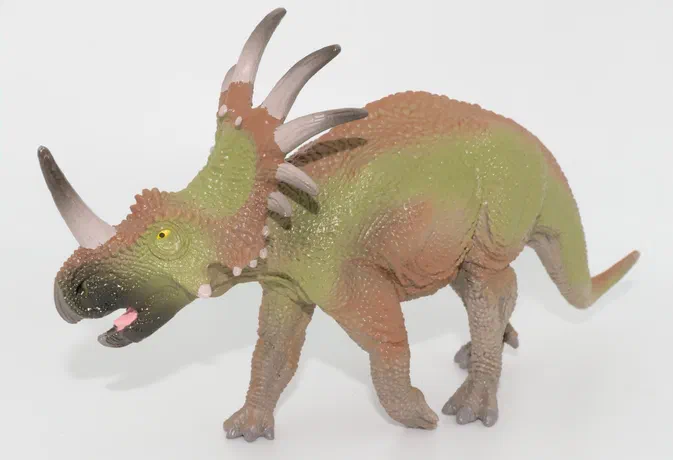 Figurine de dinosaure à cornes vert et marron sur fond blanc.