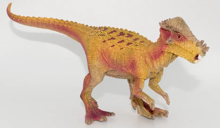 Un jouet de dinosaure jaune et rose avec des crêtes sur la tête.