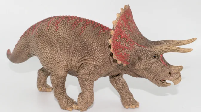 Figurine de dinosaure triceratops en position debout sur fond blanc