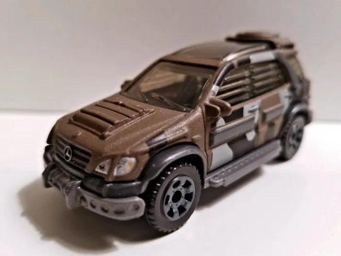 Petite voiture Matchbox Mercedes-Benz ML320 de couleur marron avec un camouflage gris et blanc.