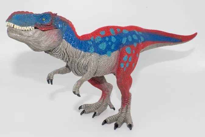 Un jouet de dinosaure à deux pattes avec un corps gris et des ailes bleues sur fond blanc.