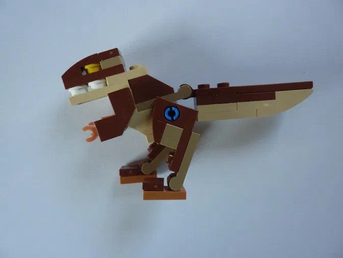 Un dinosaure T-Rex en briques LEGO marron et beige sur fond blanc.