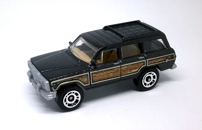 Jouet Matchbox Jeep Grand Wagoneer noir avec panneaux de bois marron et roues chromées.