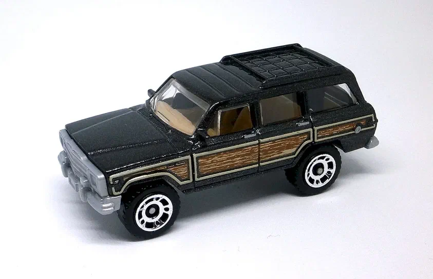 Jouet Matchbox Jeep Grand Wagoneer noir avec panneaux de bois marron et roues chromées.
