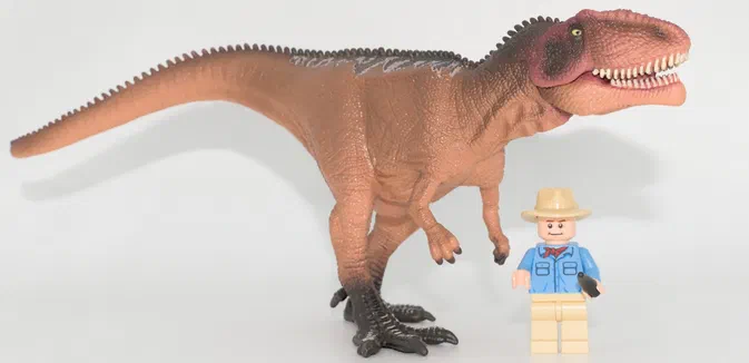 Un dinosaure T-Rex en plastique brun à côté d'un petit personnage Lego.