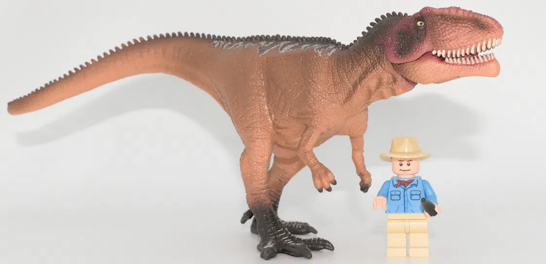 Un dinosaure T-Rex en plastique brun à côté d'un petit personnage Lego.