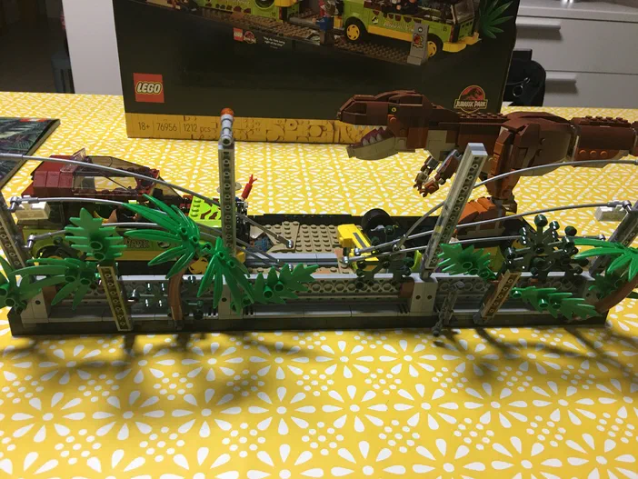 Ensemble de construction LEGO Jurassic World avec un T-Rex et une végétation peu luxuriante sur fond jaune.