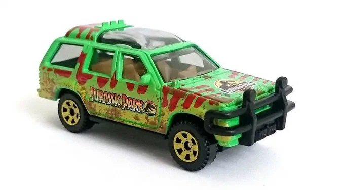 Voiture de jouet Matchbox verte avec des tampons Jurassic Park, un pare-brise fumé et une barre avant noire.