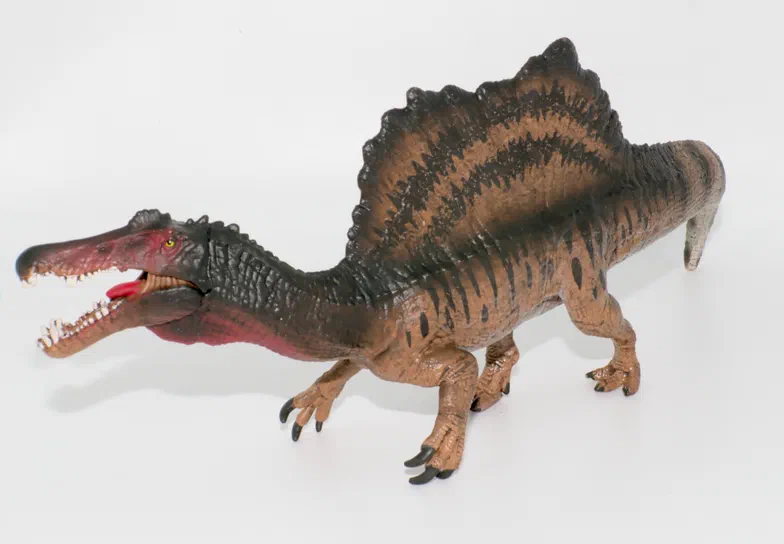 Un jouet de dinosaure Spinosaurus avec une crête dorsale proéminente et des rayures sur un fond blanc.