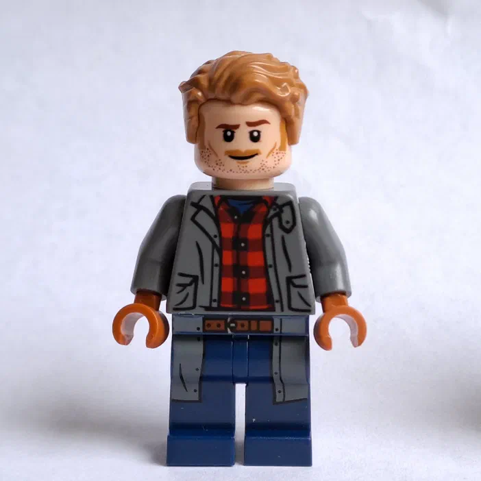 Minifigurine LEGO Jurassic World : un personnage avec des cheveux roux et une barbe poivre-sel portant une veste grise sur un t-shirt à carreaux rouges.