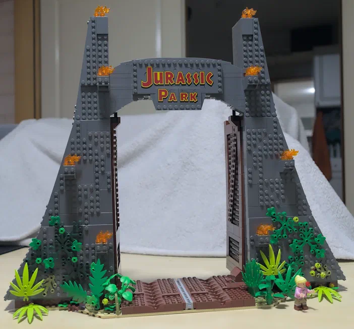 L'entrée du parc Jurassique en LEGO avec la plaque 'Jurassic Park', des plantes vertes et un petit personnage.