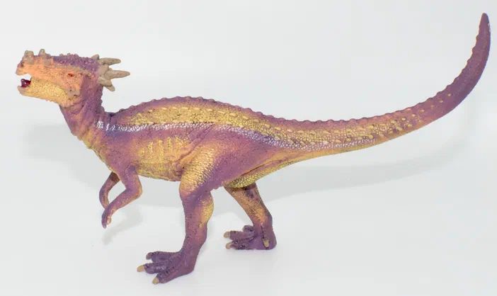 Un jouet de dinosaure à deux pattes avec une peau violette et jaune sur fond blanc.
